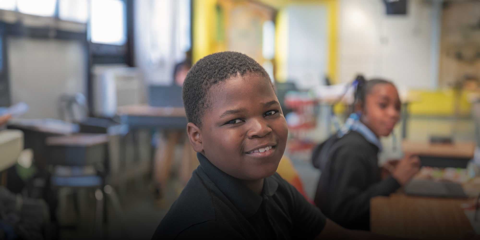 Smiling student in a black polo shirt at a classroom desk.