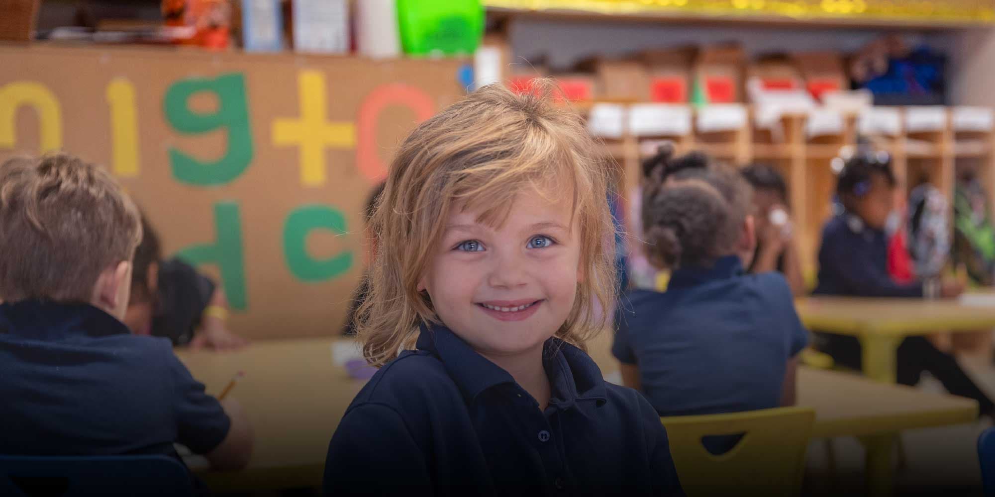 Smiling young student in a navy polo at a classroom table.