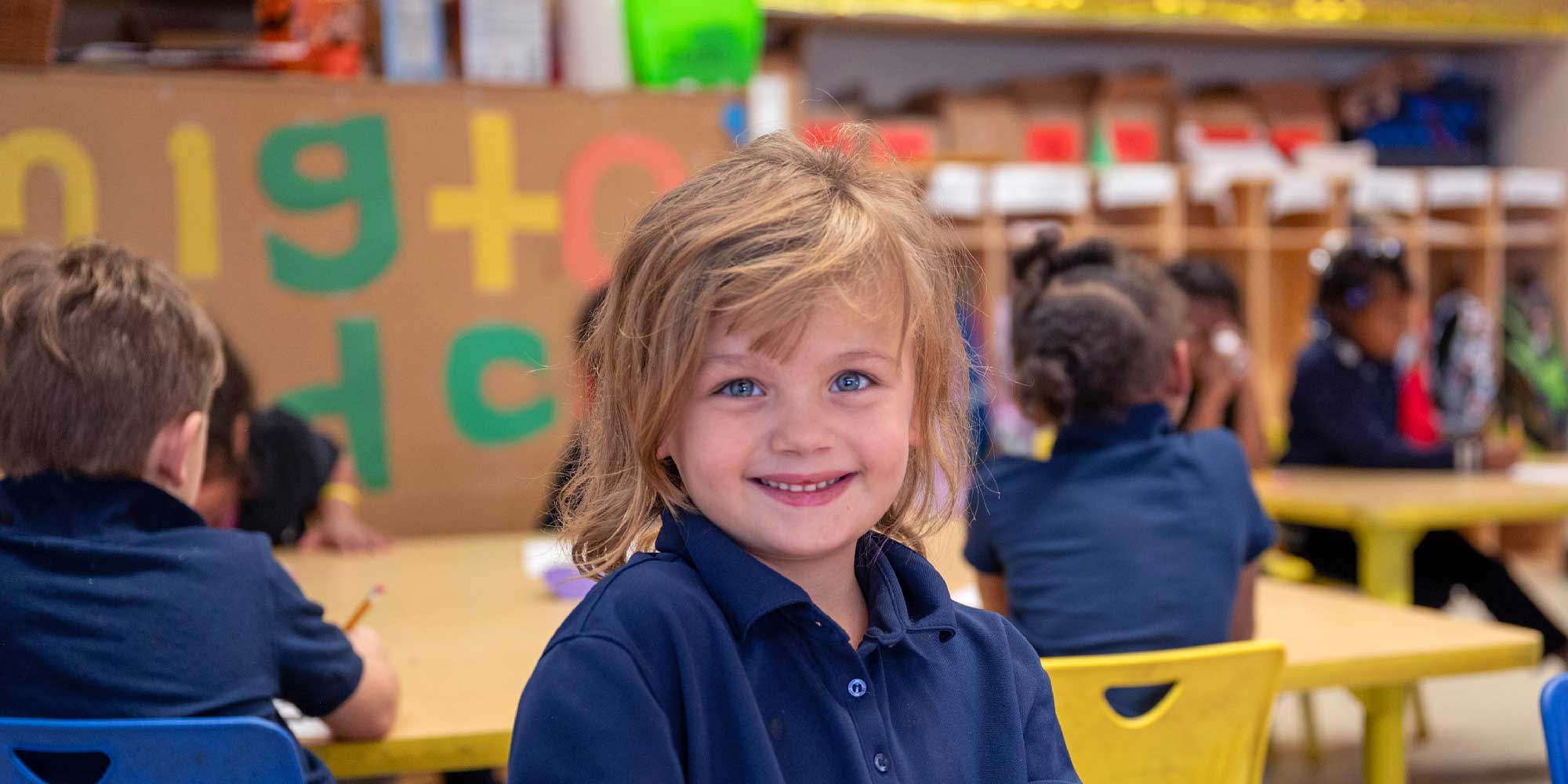 Smiling young student in a navy polo at a classroom table.