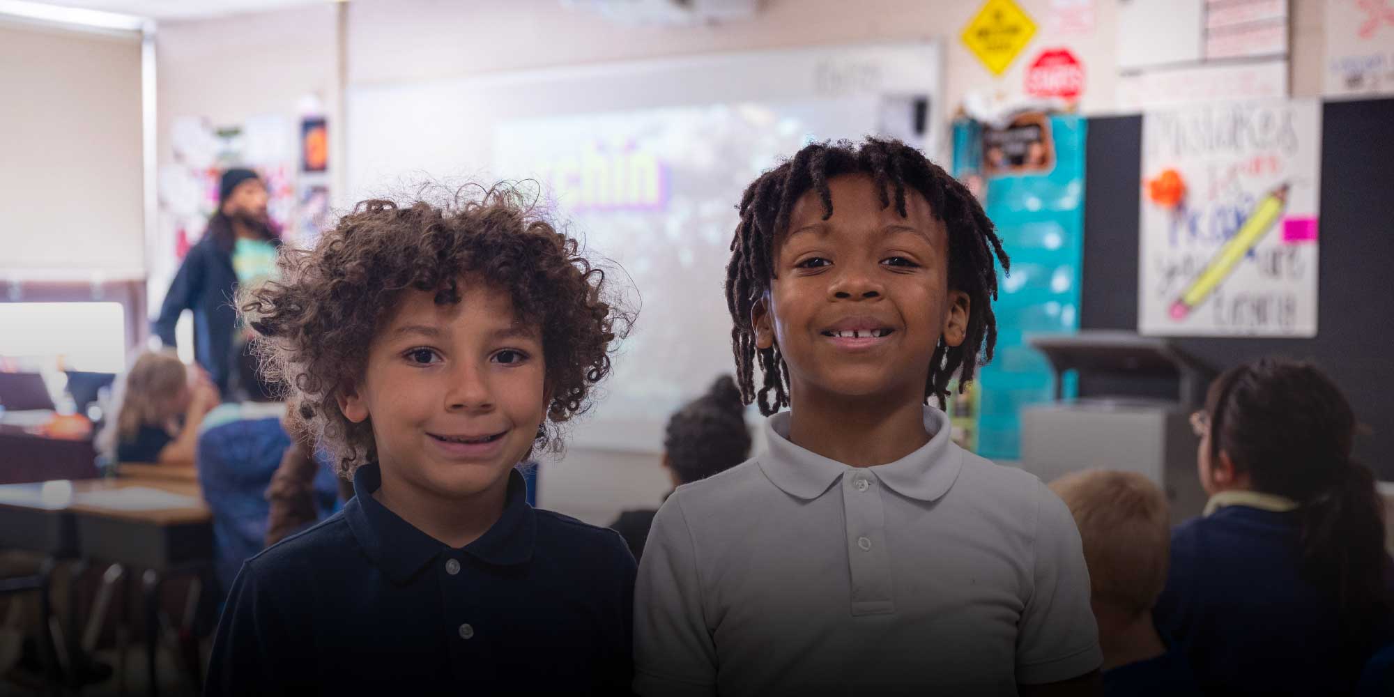 Two smiling students standing together in a classroom.